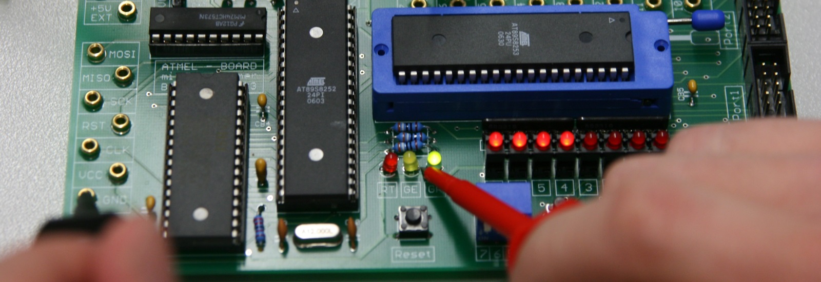 placa de circuito impresso contendo 3 processadores da Atmel, leds vermelho, amarelo e verde, teste com ponta de prova de multímetro no led amarelo